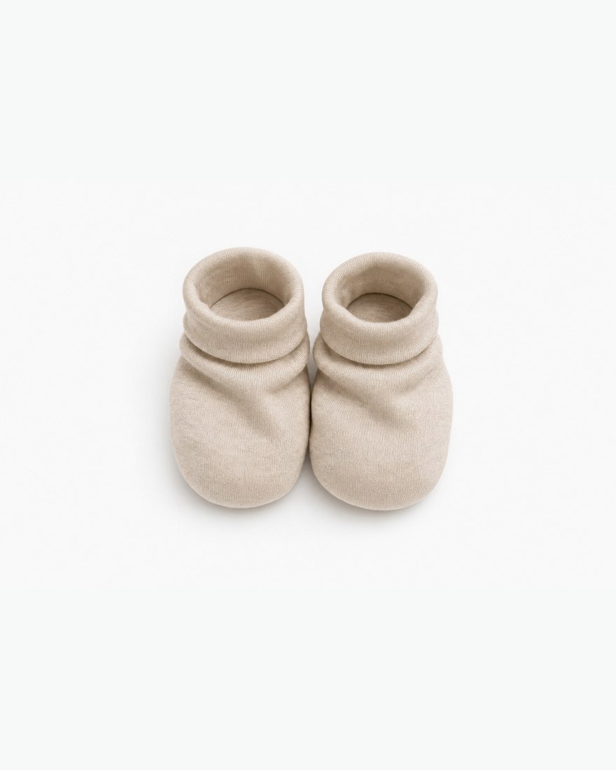 Pair of oat coloured soft bamboo newborn booties laid flat